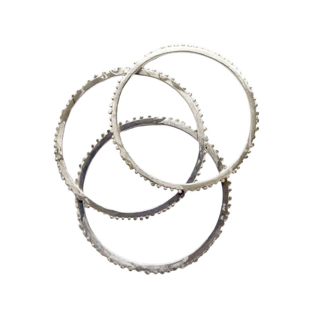 Close up of three bangles showing the side profile of the Abstract Fluid Stacking Bangle that shows how the texture is organic on each bangle